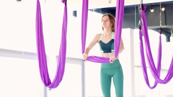 Młoda piękna kobieta ćwiczy w aero rozciągając huśtawkę. Latające ćwiczenia jogi lotniczej w fioletowym hamaku w klubie fitness — Wideo stockowe