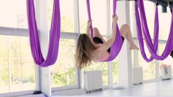 Jonge mooie vrouw oefenen in aero stretching swing opknoping ondersteboven. Luchtvliegen yoga oefeningen oefenen in paarse hangmat in fitness club — Stockvideo