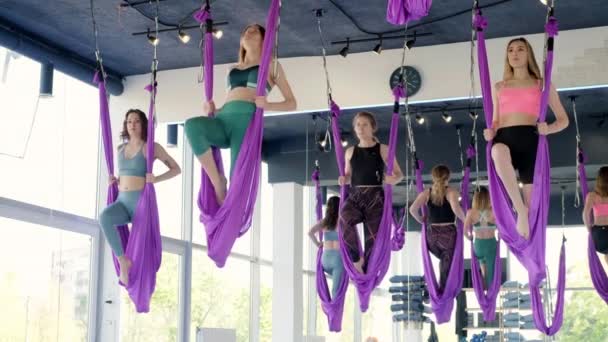 一群年轻女子练习空中伸展秋千.空中飞行瑜伽练习在健身俱乐部的紫色吊床上进行。2021年5月28日圣彼得堡俄罗斯 — 图库视频影像
