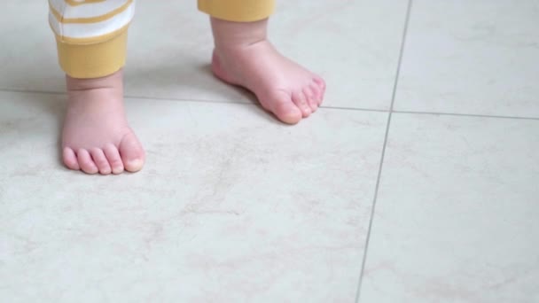 A kisfiú megteszi az első lépéseket. Felismerhetetlen kislány, aki fehér padlón sétál otthon. Mezítláb a konyhában. — Stock videók