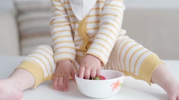 肖像画吃宝宝在家里。健康的食物，午餐时间。小孩的脸很滑稽。小孩手拿碗坐在桌子上 — 图库视频影像