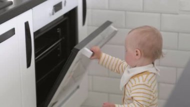 Evde, mutfakta meraklı küçük bir bebek fırını açıyor. Çocuk fırın düğmelerine basıyor. Annen için küçük bir yardımcı. Çocukların güvenliği ve korunması.