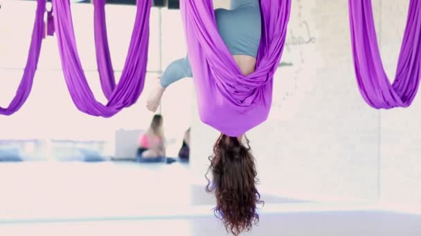 Ung kvinna öva i flygande stretching swing. Flygande yoga övningar i lila hängmatta i fitnessklubben. 28maj2021 Sankt Petersburg Ryssland — Stockvideo