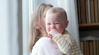 Anne kucaklıyor ve ağlayan bebeğini sakinleştiriyor. Küçük bebek ağlıyor ve anne elinin kamerasına bakıyor. Aile sevgisi.