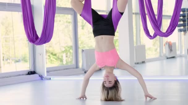 Jonge mooie vrouw oefenen in aero stretching swing opknoping ondersteboven. Luchtvliegen yoga oefeningen oefenen in paarse hangmat in fitness club — Stockvideo