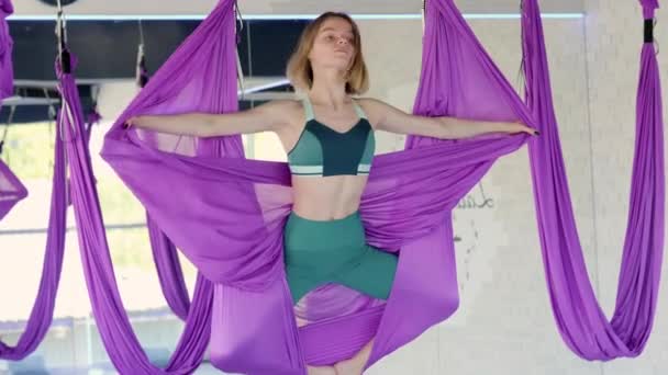 Retrato jovem sorridente mulher prática em aero alongamento swing. Exercícios de ioga de voo aéreo praticam em rede roxa no clube de fitness — Vídeo de Stock