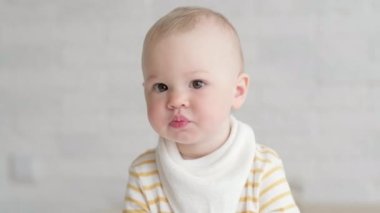 Evde portre yiyen bebek. Sağlıklı yemek, öğle yemeği zamanı. Çocuk komik suratlar yapıyor. Çocuk elinde kaseyle masada oturuyor.