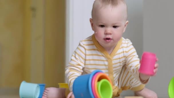 Μικρό μωρό παίζει με εκπαιδευτικά πολύχρωμα παιχνίδια στο σπίτι κάθεται στο πάτωμα. Το παιδί που διασκεδάζει κάνει πυραμίδα. Πρώιμη εκπαίδευση και ανάπτυξη. — Αρχείο Βίντεο
