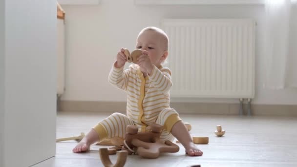 Öko Holz Spielzeug Baby-Spiel. Kleines schlaues kaukasisches Kind, das zu Hause auf dem Fußboden mit Naturspielzeug spielt. Lernspiele für die frühe Entwicklung. Kleines Kind steckt Spielzeug in den Mund — Stockvideo