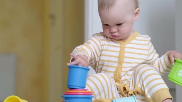 Μικρό μωρό παίζει με εκπαιδευτικά πολύχρωμα παιχνίδια στο σπίτι κάθεται στο πάτωμα. Το παιδί που διασκεδάζει κάνει πυραμίδα. Πρώιμη εκπαίδευση και ανάπτυξη. — Αρχείο Βίντεο