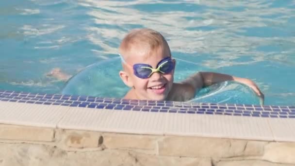 Retrato menino sorridente na piscina, criança em copos de natação e círculo de natação. Viagens de verão férias ou aulas de hotel. — Vídeo de Stock