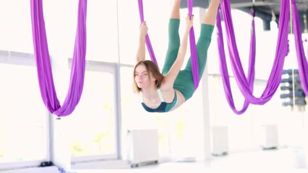 Jonge mooie vrouw oefenen in aero stretching swing. Luchtvliegen yoga oefeningen oefenen in paarse hangmat in fitness club — Stockvideo