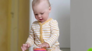 Evde renkli oyuncaklarla oynayan küçük bir bebek yerde oturuyor. Çocukların eğlenmesi piramidi oluşturur. Erken eğitim ve kalkınma.