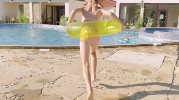 Visão traseira menina feliz correndo e saltando no anel inflável da natação na piscina, crianças que se divertem, salpicando a água. Viagens de verão família hotel férias turistas. — Vídeo de Stock