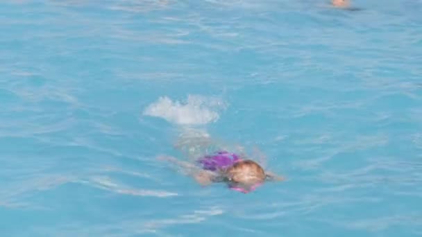 Niña pequeña en la piscina, niño divirtiéndose, sentado en el anillo de natación azul, jugando bajo el agua. Verano viajes familia hotel vacaciones turistas. — Vídeo de stock