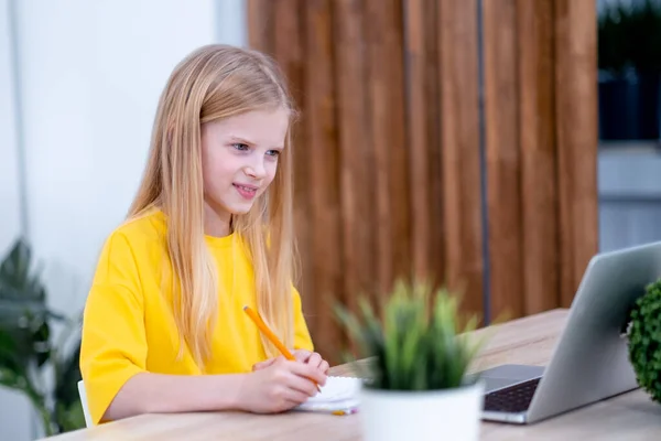 Blondynka ucząca się w domu odrabiająca lekcje z laptopem. Kształcenie online na odległość. Wracamy do szkoły. — Zdjęcie stockowe
