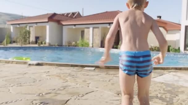 先頭へ戻る幸せな男の子を実行してプールでジャンプし、子供の楽しさを持って、水をはね。夏旅行｜家族経営のホテル休暇観光客. — ストック動画