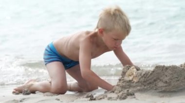 Okyanus sahilinde kumla oynayan küçük sarışın çocuk. Kızgın çocuk kumdan kale kırıyor. Aile yaz tatilleri ve sıcak ülkelere seyahatler.