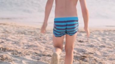 Arkaya bakan mutlu küçük çocuk yüzmek için okyanus suyuna koşar. Yaz tatili, tatil, sıcak ülkelere aile gezisi.