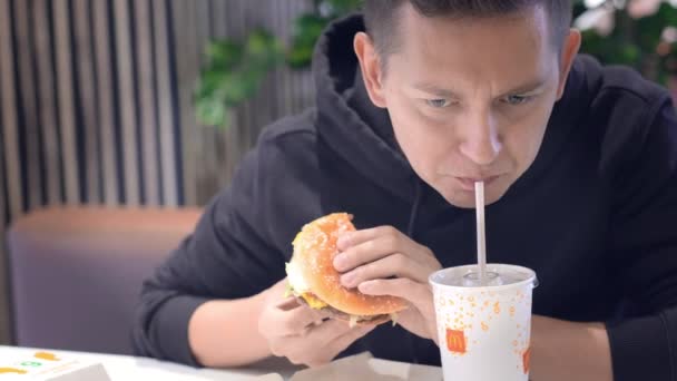 Man student eet hamburger, frietjes en drinkt cola bij McDonalds fastfood restaurant. Ongezonde voeding, snacks, junkfood. 26augustus 2021 Sint-Petersburg Rusland — Stockvideo