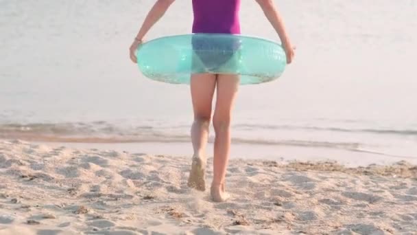 Arkaya bakan mutlu küçük kız şişme yüzme halkasıyla yüzmek için okyanus suyuna koşuyor. Yaz tatili, tatil, sıcak ülkelere aile gezisi. — Stok video