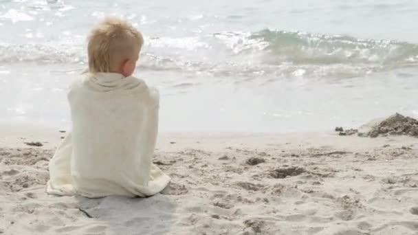Little boy sitting wrapped in towel on ocean shore beach after swimming in sea. Summer vacation, holiday, family trip to warm countries — Stock Video