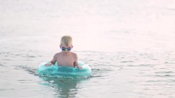 Menino sai da água do mar, criança se divertindo, nadando no anel de natação azul. Férias de verão, férias, viagem em família para países quentes — Vídeo de Stock