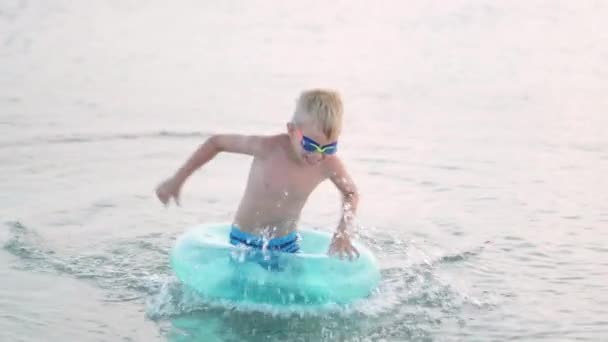 Le petit garçon sort de l'eau de mer, l'enfant s'amuse, nage sur l'anneau de natation bleu. Vacances d'été, vacances, voyage en famille dans des pays chauds — Video