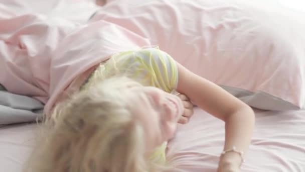 Porträtt stilig söt liten blond flicka har roligt i sängen på morgonen. Förtjusande unge som snurrar, skrattar, ligger upp och ner — Stockvideo