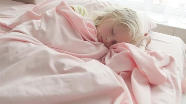 Förtjusande blond flicka sover sött på morgonen på rosa sängkläder hemma. Barndrömmar, komfort, vila och ro — Stockvideo