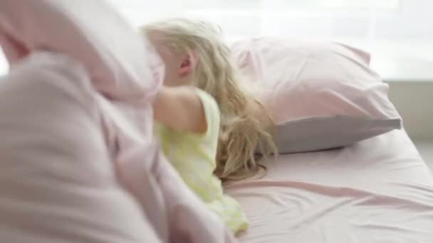 Retrato bonito menina loira bonito se divertindo na cama pela manhã. Criança adorável girando, rindo, deitado de cabeça para baixo — Vídeo de Stock