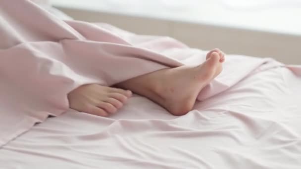 Sluiten Kid voeten steken uit van onder de deken in de ochtend licht. Lichaamsbenen in bed. Ontwaken Voet Slapen Ontspannen Concept. — Stockvideo