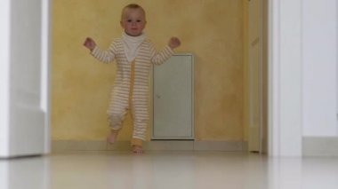 Bebek ilk adımı atıyor. Evde beyaz zeminde koşan küçük kız ya da oğlan. Mutfakta çıplak ayaklı çocuk..
