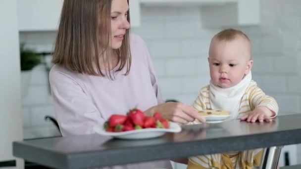 Moeder en baby koken thuis in de keuken. Gezond eten, lunchtijd. Kind het kind kiest wat te eten koekjes of aardbeien — Stockvideo