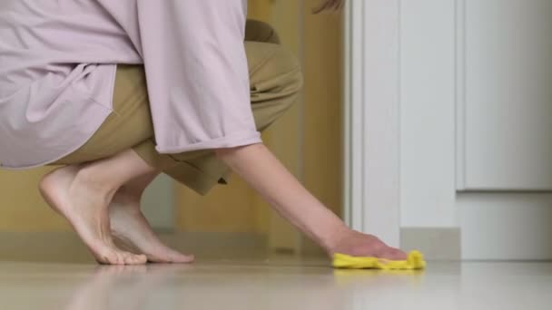 Maman pieds nus essuie le sol de la cuisine avec du tissu jaune après que l'enfant renverse la nourriture. Propreté, nettoyage et hygiène dans la maison avec bébé. — Video