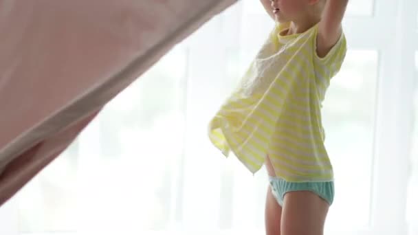 Gülümseyen küçük sarışın kız sabahları evde yatak yapıyor. Çocuk battaniyeyi yaymak için sallıyor. Temiz çarşaf. Günlük rutinler — Stok video