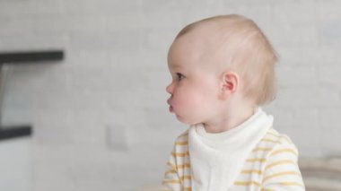 Evde portre yiyen bebek. Sağlıklı yemek, öğle yemeği zamanı. Çocuk komik suratlar yapıyor. Çocuk elinde kaseyle masada oturuyor.