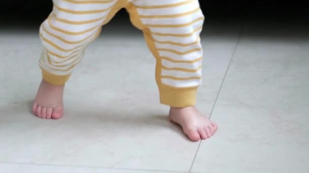 A kisfiú megteszi az első lépéseket. Felismerhetetlen kislány, aki fehér padlón sétál otthon. Mezítláb a konyhában. — Stock videók