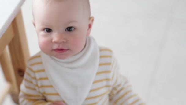 Portrait of curious child at home. Little baby peeks out from the table in kitchen and looks into camera. Happy childhood, games at home — Stock Video