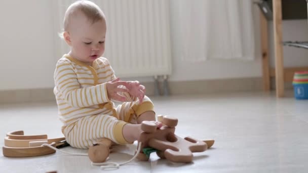 Eco juguete de madera juego de bebé. Pequeño niño caucásico inteligente jugando juguetes naturales en el suelo en casa. Juegos educativos para el desarrollo temprano. Pequeño niño pone juguete en su boca — Vídeo de stock