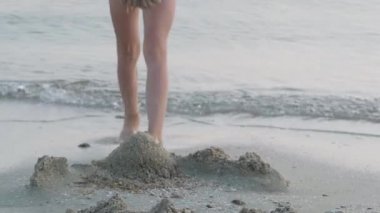 Gün batımında kumsalda kumla oynayan küçük sarışın kız. Çocuk kumdan kale inşa ediyor. Aile yaz tatilleri ve sıcak ülkelere seyahatler.