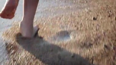 Çocuk ayakları plaj suyunda güneş ışınları altında koşuyor. Yaz tatili, tatil, aile gezisi.