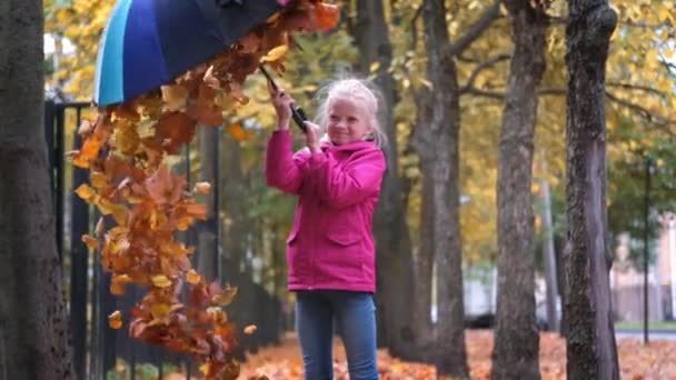 Petite fille jouant avec les feuilles tombées d'automne dans le parc. Enfant riant vomissant des feuilles d'érable orange doré — Video