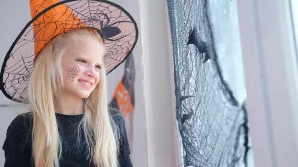 4k. Šťastná dívka v kostýmu čarodějnice připravuje na Halloween zdobení okna v pokoji černými netopýry — Stock video