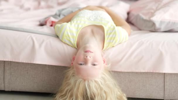 Портрет красивый симпатичный маленький блондинка весело в постели по утрам. Очаровательный ребенок кружится, смеется, лежит вверх ногами — стоковое видео