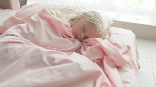 Schattig blond meisje slaapt 's morgens zoet op roze beddengoed thuis. Kinderdromen, comfort, rust en vrede — Stockvideo