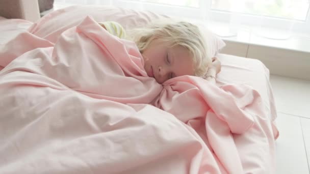 Förtjusande blond flicka sover sött på morgonen på rosa sängkläder hemma. Barndrömmar, komfort, vila och ro — Stockvideo