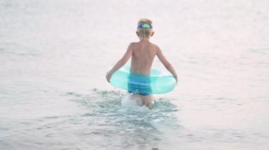 Küçük çocuk okyanus suyunda oynuyor, çocuk eğleniyor, mavi yüzme ringinde yüzüyor. Yaz tatili, tatil, sıcak ülkelere aile gezisi.