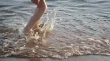 Gün batımında çıplak ayaklı çocukların ayakları kumsalda okyanus kıyısında koşuyor. Yaz tatili, tatil, aile gezisi. Sıcak ülkelere turizm