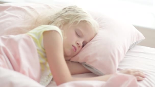 Adorable fille blonde dormant doucement le matin sur des draps roses à la maison. Rêves d'enfants, confort, repos et paix — Video